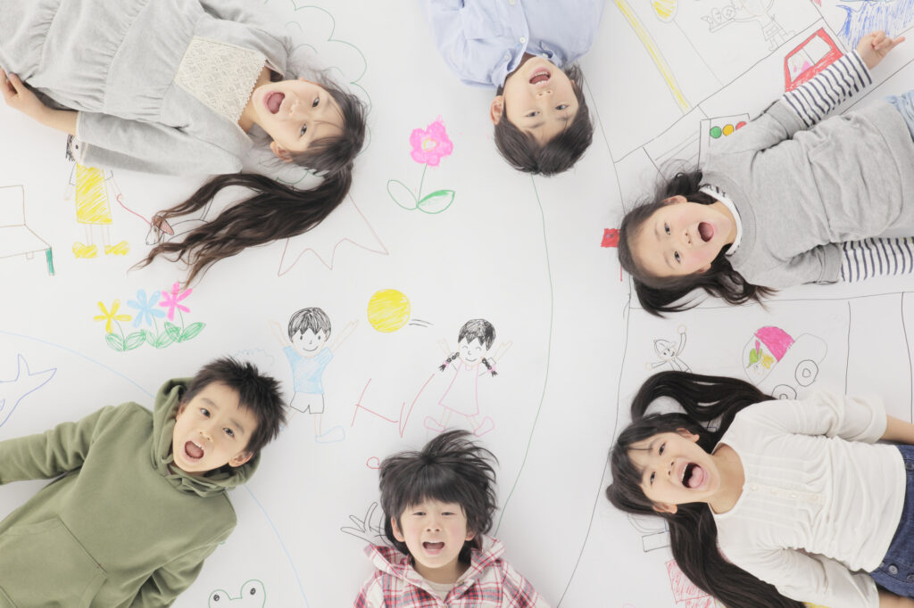 子どもが円形に寝て真上についてるカメラを笑顔で見ている様子